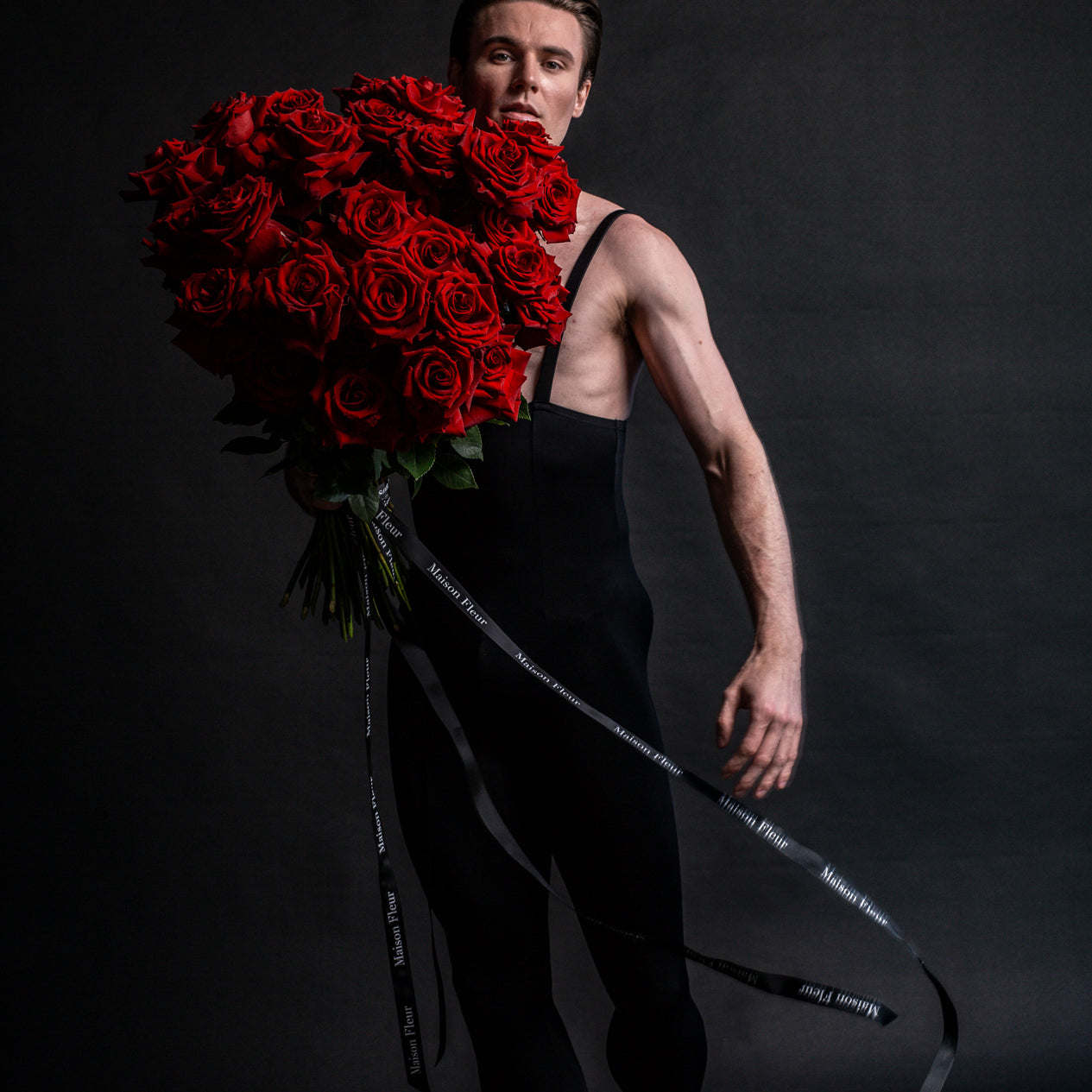 Male Ballerina wearing black holding a large bouquet of red roses
