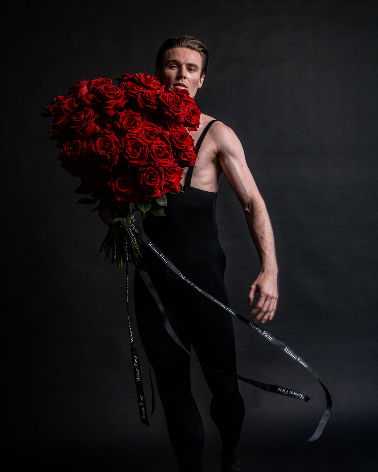 Male Ballerina wearing black holding a large bouquet of red roses
